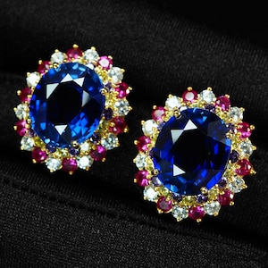 Può includere: Un paio di orecchini con zaffiro blu taglio ovale incastonato in oro. Ogni pietra centrale blu è circondata da un alone di rubini rossi, diamanti bianchi trasparenti e zaffiri gialli più piccoli, creando un vivace design floreale.