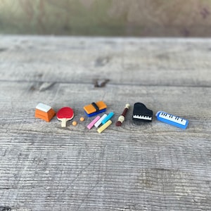 May include: A collection of miniature clay objects representing various hobbies and activities, including a piano, a ping pong paddle, a book, a flute, and a set of chalk.