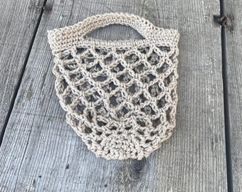 May include: A beige crocheted mesh bag with a handle. The bag is made of natural fibres and has a delicate, open weave.