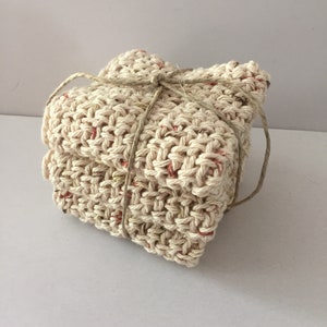 May include: A stack of three beige knitted dishcloths with red flecks, tied together with twine.