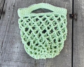 May include: A light green crocheted mesh bag with a handle. The bag is made of a soft, lightweight material and is ideal for carrying small items.