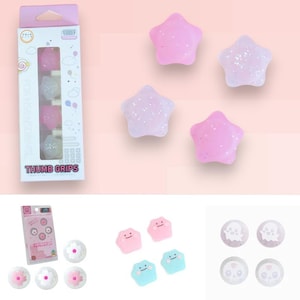 Puede incluir: Un paquete de agarres para pulgar con el texto "THUMB GRIPS" y varios agarres en forma de estrella y flor en rosa, blanco y azul. Algunos agarres tienen purpurina.