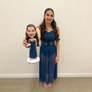 May include: A custom bobblehead of a woman in a blue dress, holding a bouquet of flowers. The bobblehead is on a white base with the text "Samma, Senior Dance 2023". The woman in the image is wearing a matching blue dress.