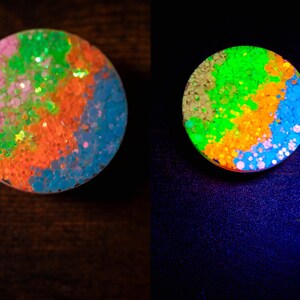 May include: A round, colorful accessory with a glittery, abstract design. The design features pink, green, orange, and blue sections. The accessory glows brightly under a black light, showcasing the vibrant colors.