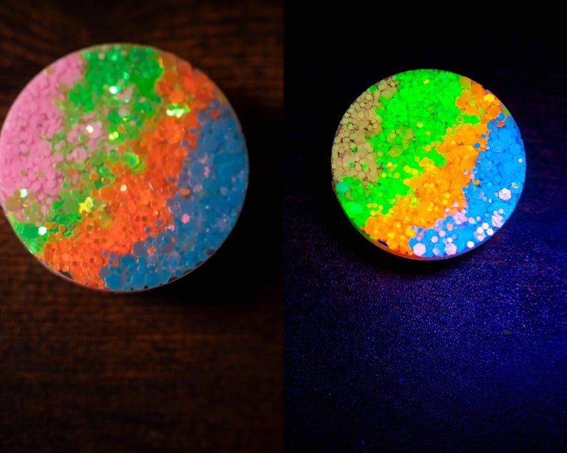 May include: A round, colorful accessory with a glittery, abstract design. The design features pink, green, orange, and blue sections. The accessory glows brightly under a black light, showcasing the vibrant colors.