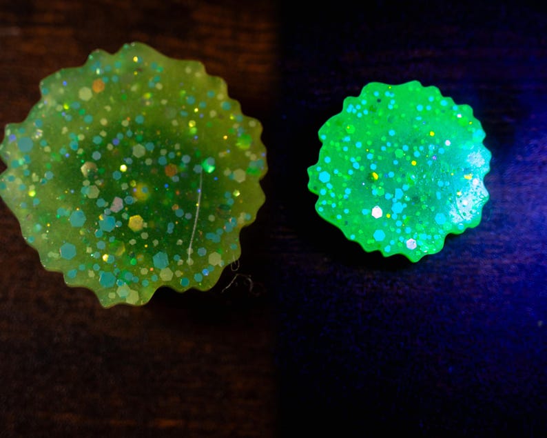 May include: Two round, lime green resin objects with a scalloped edge. The objects are filled with iridescent glitter in various shapes and sizes. One object glows bright green, while the other appears less vibrant.
