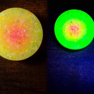 May include: Two round, glittery objects. One is yellow with a pink center, the other glows bright green with a yellow and pink center. The objects are likely decorative or functional items, possibly for crafts or home decor.