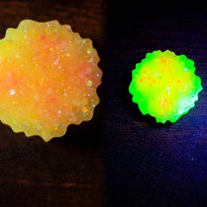 May include: Two resin pieces with a scalloped edge. One is yellow with orange and glitter, the other is neon green. The pieces are on a dark surface. The yellow piece has a glittery, speckled appearance.