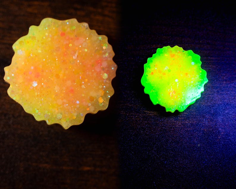 May include: Two resin pieces with a scalloped edge. One is yellow with orange and glitter, the other is neon green. The pieces are on a dark surface. The yellow piece has a glittery, speckled appearance.