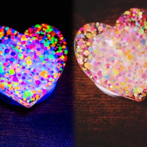 May include: Two heart-shaped objects, one glowing with neon colors and the other with pastel confetti. The neon heart has a blue base and is filled with colorful dots. The other heart has a clear base with pastel confetti.