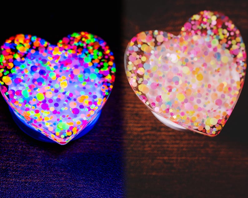 May include: Two heart-shaped objects, one glowing with neon colors and the other with pastel confetti. The neon heart has a blue base and is filled with colorful dots. The other heart has a clear base with pastel confetti.