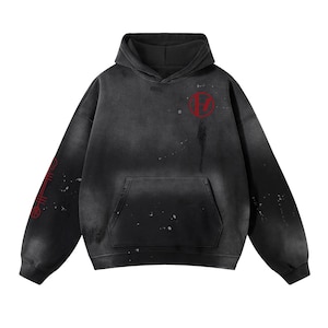 Puede incluir: Sudadera con capucha negra y gris con un aspecto desgastado y vintage. Presenta un logotipo circular rojo en el pecho y texto rojo en la manga izquierda. Incluye un bolsillo delantero y una capucha. La sudadera tiene un diseño descolorido y moteado.
