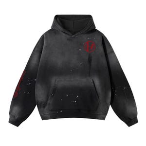 May include: A black hooded sweatshirt featuring a faded, washed-out aesthetic with white paint splatter details. A red circular logo is printed on the upper left chest, and a red vertical graphic symbol is displayed on the right sleeve.