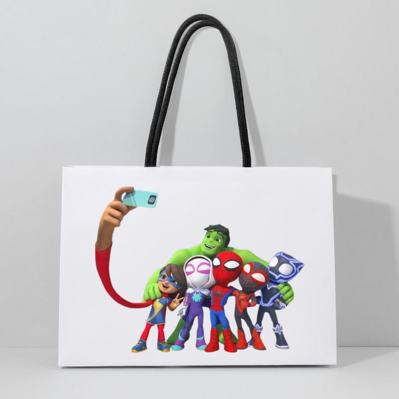 May include: White tote bag with black handles. The bag features a group of cartoon superheroes, including Spider-Man and Hulk, taking a selfie. The superheroes are in colourful costumes. The bag is rectangular and has a simple design.