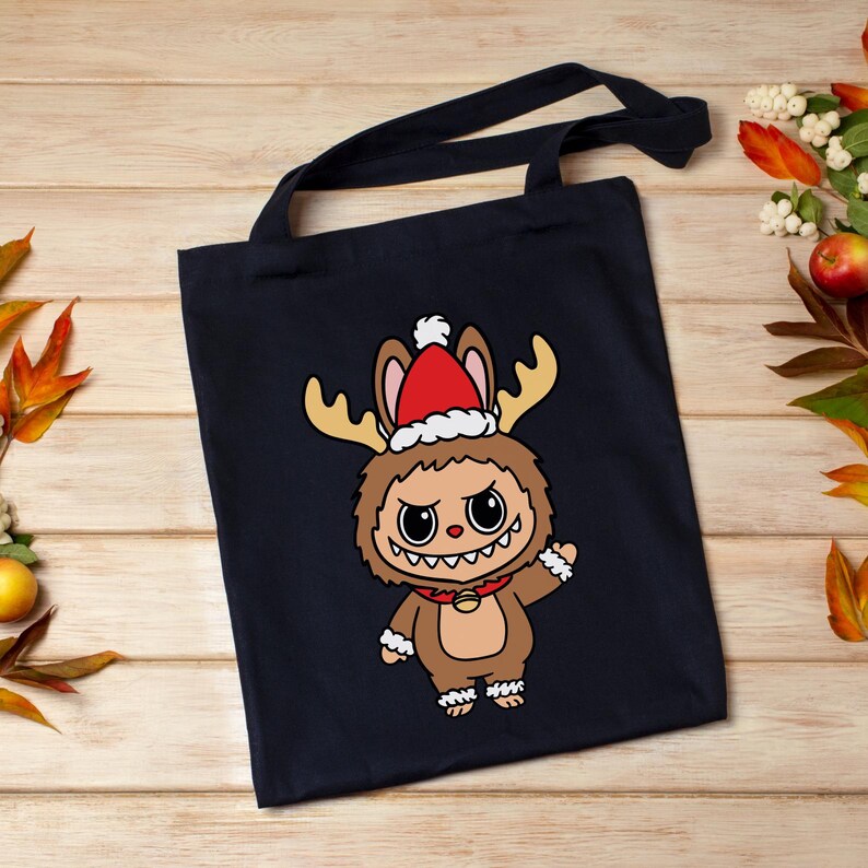 May include: A navy blue tote bag featuring a cartoon character dressed as a reindeer with a Santa hat. The character has large eyes, a toothy grin, and is wearing a red collar with a gold bell. The bag has long black handles.