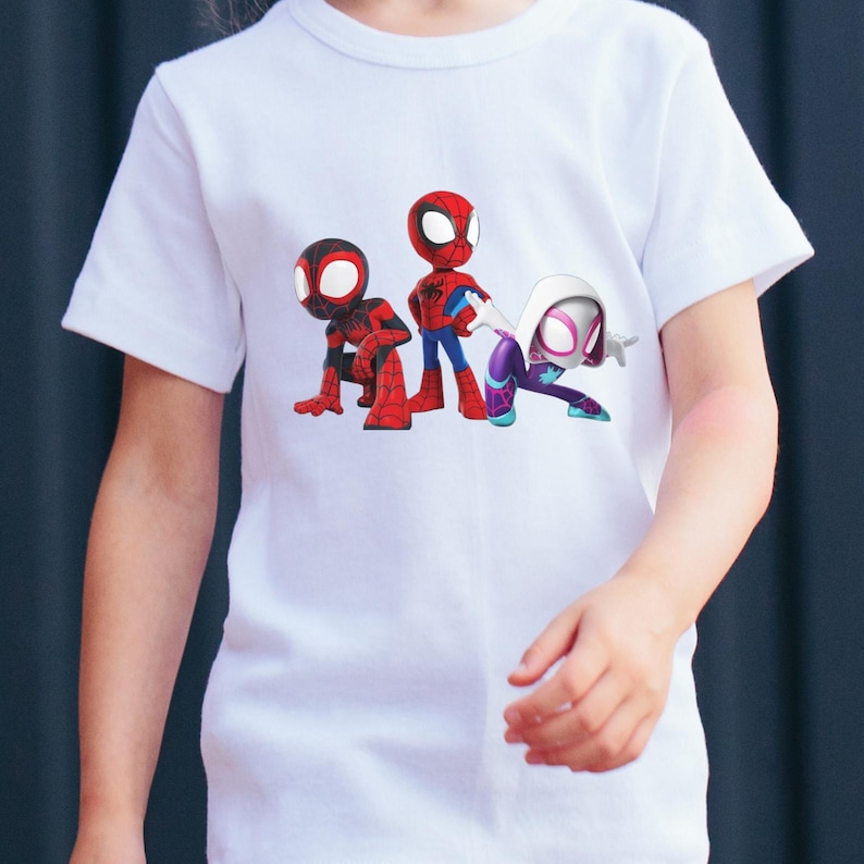May include: White t-shirt with a vibrant graphic of three Spider-Man characters. The characters are depicted in red, blue, purple, and white. The t-shirt is made of a soft, lightweight material.