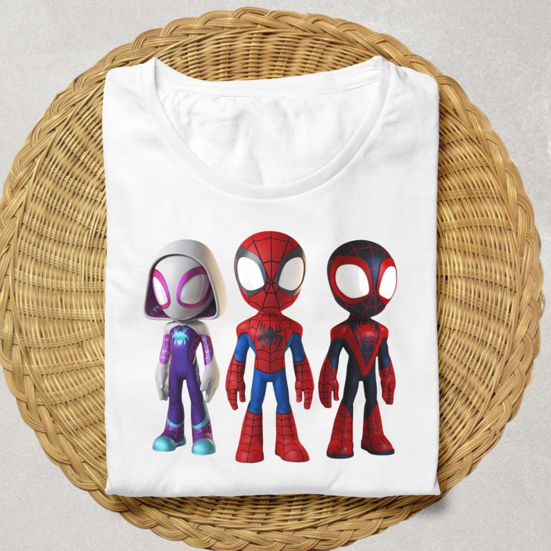May include: White t-shirt with three cartoon Spider-Man characters: Spider-Gwen in purple, Spider-Man in red and blue, and Miles Morales in black and red. The shirt is folded on a woven, circular surface, likely a placemat or basket.