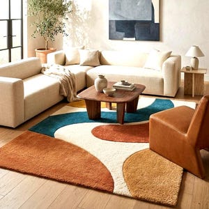 May include: A rectangular area rug featuring a textured, abstract pattern with large, curved shapes in shades of burnt orange, mustard yellow, teal, and cream. The rug has a thick, plush pile and is positioned on a light-colored wooden floor.