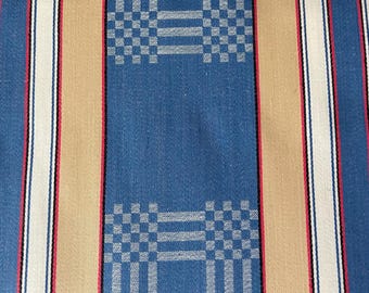 May include: A woven fabric featuring a repeating pattern of vertical stripes in blue, tan, and white. The blue sections are accented with a small, light blue checkered grid design, while thin red and black lines border the white stripes.