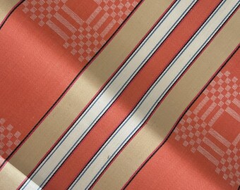 May include: A woven fabric featuring a repeating pattern of wide coral orange bands and tan stripes. The coral sections are decorated with a white geometric grid motif, while the tan stripes are accented by thin black and white pinstripes.