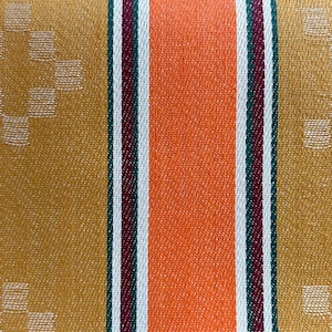 Puede incluir: Una tela tejida con rayas verticales en naranja, amarillo mostaza, rojo oscuro y blanco. Las secciones de color amarillo mostaza están decoradas con un patrón geométrico repetitivo de diamantes hecho de pequeños cuadrados claros.