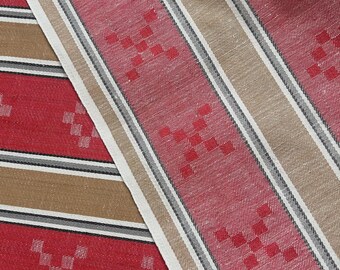 May include: A woven fabric featuring alternating vertical stripes in red and tan. The red sections are decorated with a repeating pattern of small, red, pixelated cross shapes. Thin black and white pinstripes separate the main color bands.