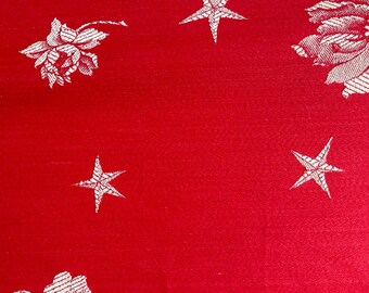 May include: A vibrant red fabric featuring a woven pattern of white five-pointed stars and detailed floral blossoms. The design is repeated across the surface, showcasing a contrast between the bold red background and the white textile elements.