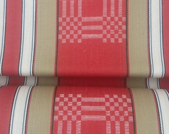 May include: A woven fabric featuring a repeating pattern of wide red bands with a checkered grid design, separated by vertical stripes in beige, white, and thin blue lines. The textile displays a structured, symmetrical layout with alternating color blocks.