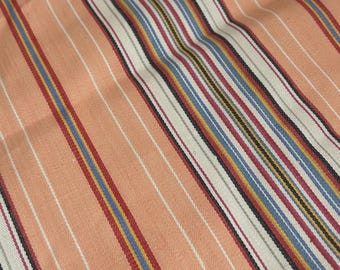 May include: A woven fabric featuring a repeating pattern of diagonal stripes in shades of peach, cream, light blue, dark red, yellow, and black. The texture shows a visible weave with consistent line spacing across the entire surface of the material.