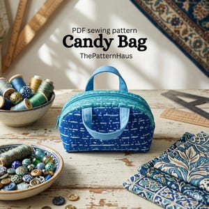 Op de afbeelding: Een blauw-witte Candy Bag, een PDF-naaipatroon van ThePatternHaus, met een ritssluiting en een handvat. De tas is omgeven door naaimaterialen, waaronder garen, knopen en stof.