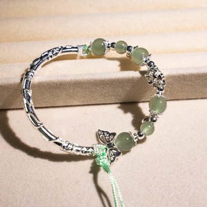 Puede incluir: Pulsera de plata con diseño de mariposa y flores. La pulsera incorpora cuentas redondas de color verde claro y un cierre plateado decorativo. Una delicada pieza de joyería.