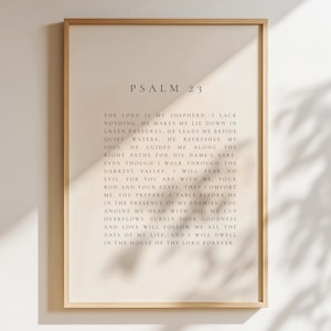 Puede incluir: Impresión enmarcada con el texto del Salmo 23. El texto negro en fuente serif está sobre un fondo crema, dentro de un marco de madera marrón claro. La impresión se presenta contra una pared neutra, con sombras.