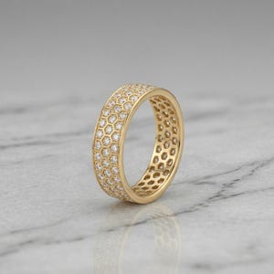 May include: A gold ring with a honeycomb design, encrusted with small, sparkling diamonds. The ring is set against a neutral background, highlighting its intricate details and radiant appearance. A luxurious piece of jewelry.