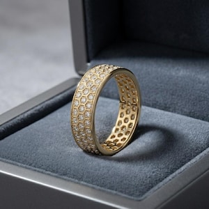 May include: A gold ring with a honeycomb design, encrusted with small, sparkling diamonds. The ring is displayed inside a gray jewelry box, showcasing its intricate details and luxurious appearance. The ring's band is approximately 0.5 inches wide.