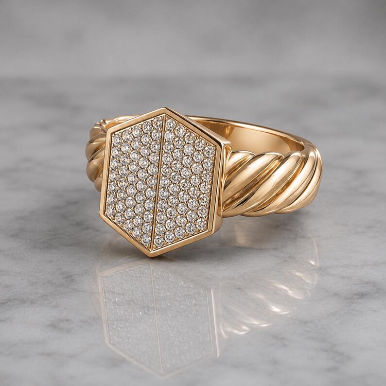 May include: A gold ring with a hexagonal face encrusted with small, sparkling stones. The ring's band features a twisted rope design. The ring is set against a light, reflective surface.
