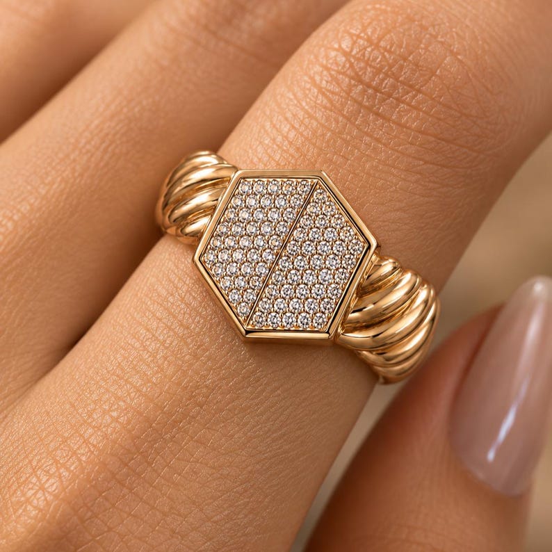 May include: A gold ring with a hexagonal face, encrusted with small, sparkling stones. The ring's band features a ribbed design, adding texture and visual interest. The ring is a piece of jewelry.