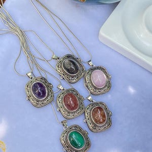 Peut inclure: Un ensemble de six colliers argentés, chacun doté d'un pendentif en pierre ovale serti dans un cadre en métal orné de filigrane. Les pierres incluent de l'améthyste violette, du quartz rose, de la malachite verte et diverses pierres brunes et grises.