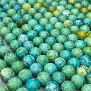 May include: A large collection of round, polished beads in various shades of turquoise, teal, and lime green. Each bead features unique natural marbling, speckles, and color variations, creating a textured, multi-tonal appearance across the group.