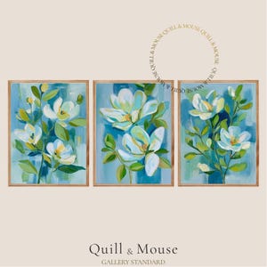 May include: Set of three framed floral art prints. Each print features white and yellow flowers with green leaves against a blue and teal background. The frames are a light brown color. The text "Quill & Mouse" and "Gallery Standard" are at the bottom.