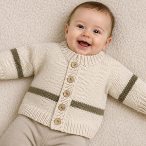 Peut inclure: Un gilet en tricot couleur crème pour nourrisson avec une encolure ronde, des manches longues ornées d'une rayure horizontale vert olive et cinq boutons en bois brun clair sur le devant. Le vêtement présente des poignets et un ourlet côtelés.