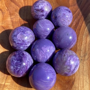 May include: Nine polished purple spheres with swirling patterns and a glossy finish. The spheres are arranged on a wooden surface, highlighting their colour variations and textures. Each sphere is approximately 3.8 cm in diameter.