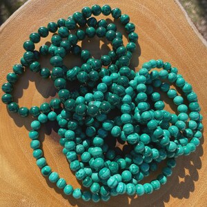 Puede incluir: Varias pulseras de cuentas de piedra malaquita. Las cuentas son de un color verde intenso y moteado, con variaciones de tono y patrón. Las pulseras están dispuestas de forma suelta y superpuesta, mostrando la belleza natural de las piedras.