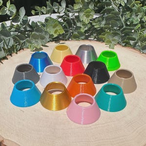 May include: A collection of colorful, cone-shaped objects in various hues, including blue, yellow, red, and pink. The objects are arranged on a wooden surface, with a natural wood grain pattern. The objects appear to be 3D-printed.