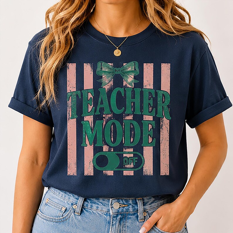May include: Navy blue t-shirt with a distressed pink and white striped design. The shirt features the text "TEACHER MODE" in green, with a green bow and a switch graphic that says "OFF".