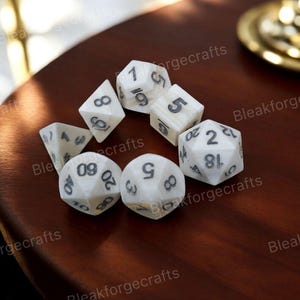 May include: A collection of white, multi-sided dice with black numbering, arranged on a dark wooden surface. The dice are of various shapes, including D4, D6, D8, D10, D12, and D20, commonly used in tabletop role-playing games.