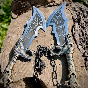 May include: Two silver and blue fantasy blades with intricate designs and dragon-head handles are connected by a black chain. The blades have a curved shape with a light blue edge and detailed engravings.