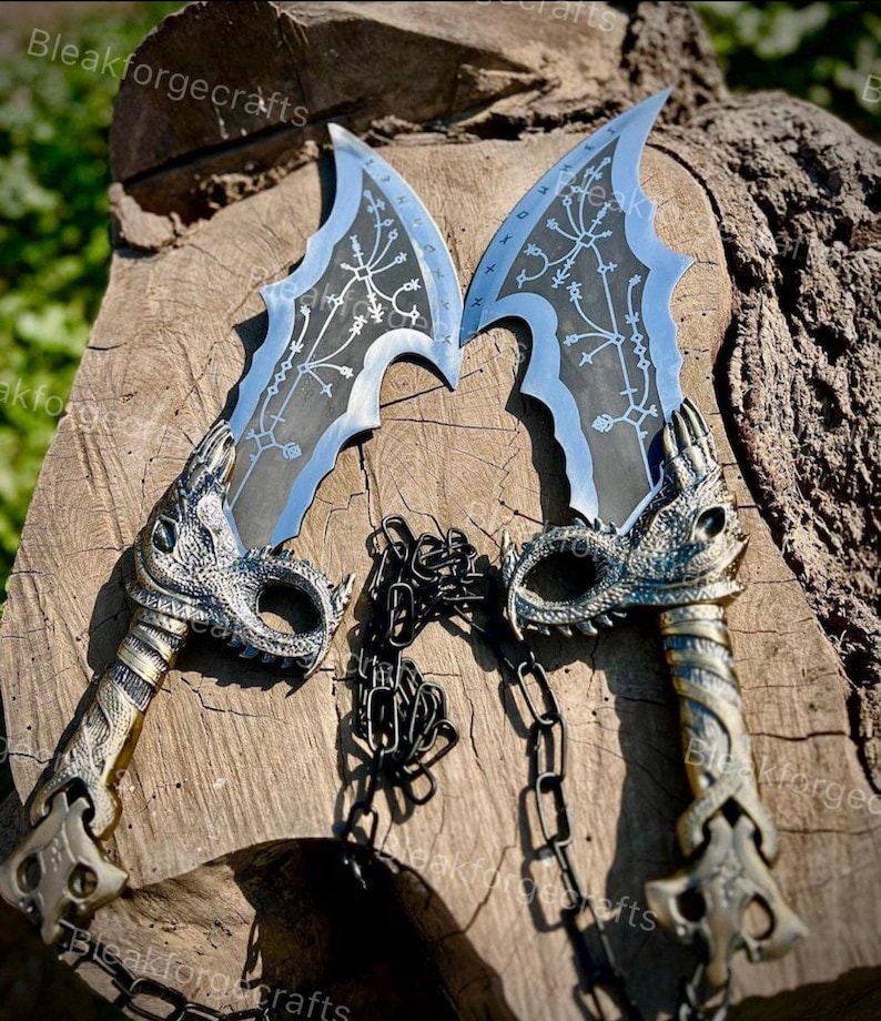 May include: Two silver and blue fantasy blades with intricate designs and dragon-head handles are connected by a black chain. The blades have a curved shape with a light blue edge and detailed engravings.