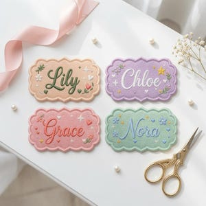 May include: Four rectangular embroidered patches with scalloped edges, each featuring a unique name in cursive script: Lily in dark green, Chloe in white, Grace in coral, and Nora in blue, surrounded by small floral and star motifs.