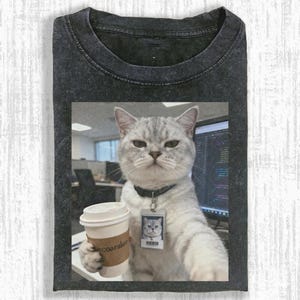 Könnte beinhalten: Dunkelgraues T-Shirt mit einer Grafik einer grauen Katze, die eine Kaffeetasse hält und einen Ausweis trägt. Die Katze befindet sich in einer Büroumgebung. Auf dem Kaffeebecher steht der Text "ecoaralon".