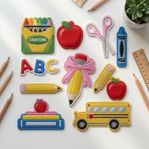 May include: A collection of school-themed embroidered patches including a box of crayons labeled CRAYONS, a red apple, pink scissors, a blue crayon, ABC letters, a pencil with a pink bow, a yellow pencil, a second apple, books, and a yellow school bus.